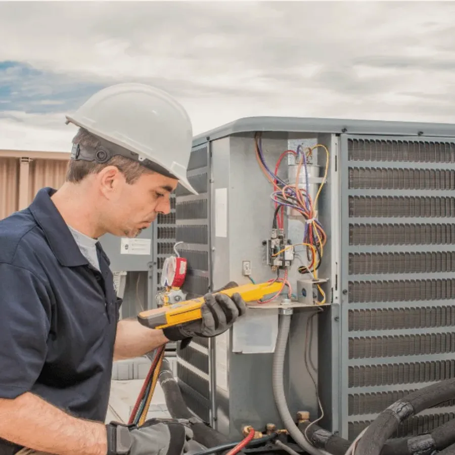 HVAC technician in a hard hat testing an outdoor air conditioner with a multimeter